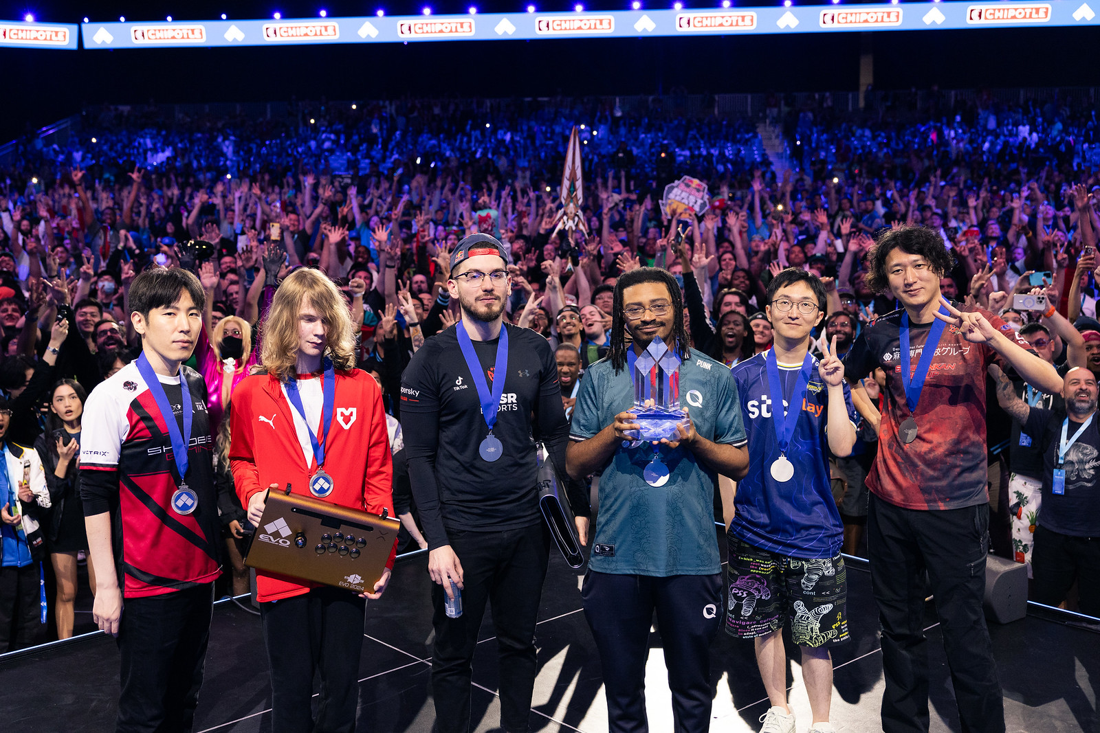 Esports finalists pose with medals and a trophy.