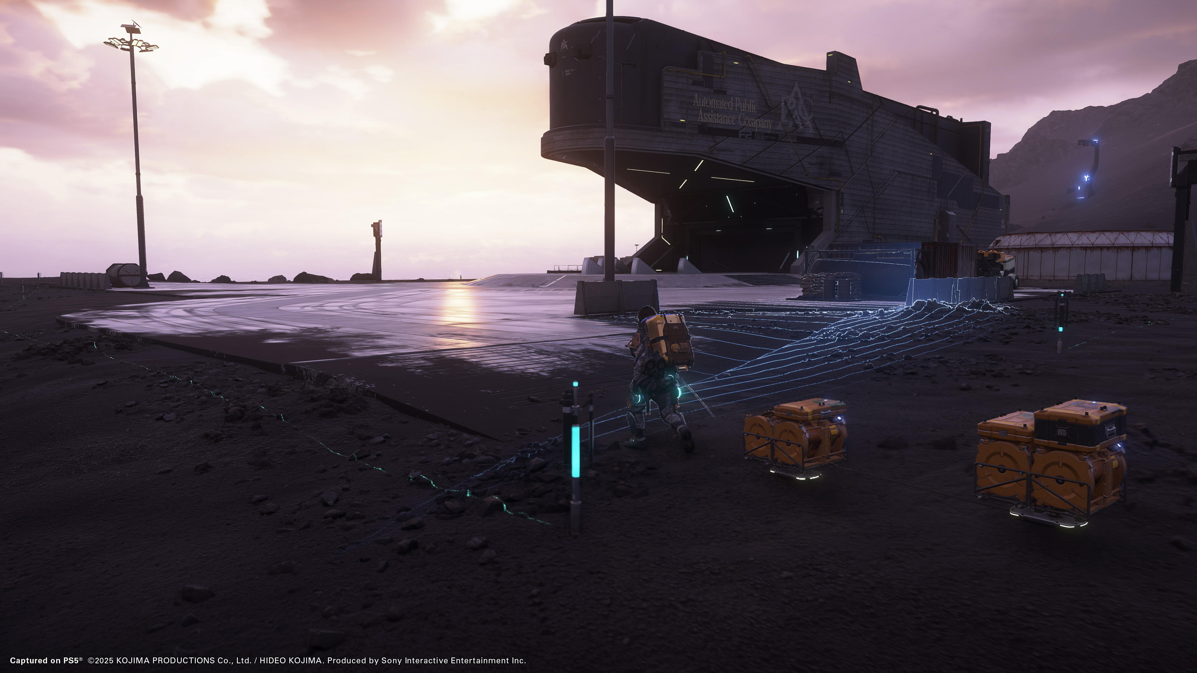 Death Stranding 2: On the Beach screenshot showing Sam approaching a facility with cargo behind him